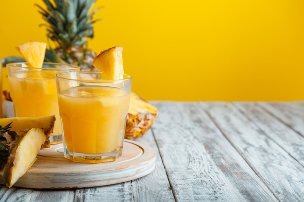 Tasty pineapple juice in glass with ingredients on white wooden table with yellow summer background. Fresh natural pineapple juice cocktail and juice Glass with copy space. High quality stock photo.
