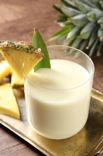 tasty pineapple smoothie in glass and fresh fruit on wooden table closeup