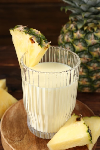 tasty pineapple smoothie in glass and slices of fruit on wooden table closeup