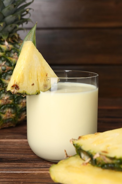 tasty pineapple smoothie in glass and slices of fruit on wooden table closeup