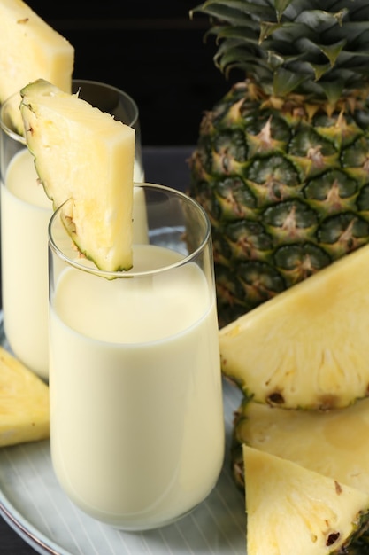 tasty pineapple smoothie in glasses and fruit on black background closeup