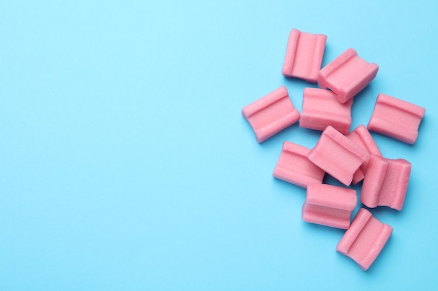 Tasty pink chewing gums on light blue background flat lay Space for text