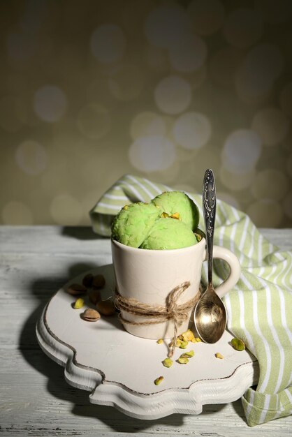 Tasty pistachio ice cream in cup on wooden table on light background