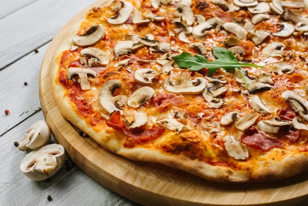 Tasty pizza Caprizzioza with tomato sauce, ham and champignons on the white wooden background