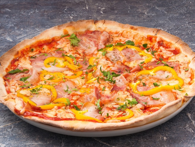 Tasty pizza with bacon and bell pepper, tomato sauce, decorated with greens