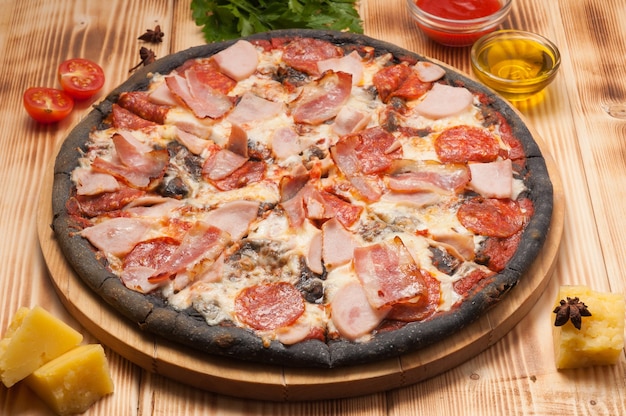 Tasty pizza with pepperoni ham and bacon on black dough