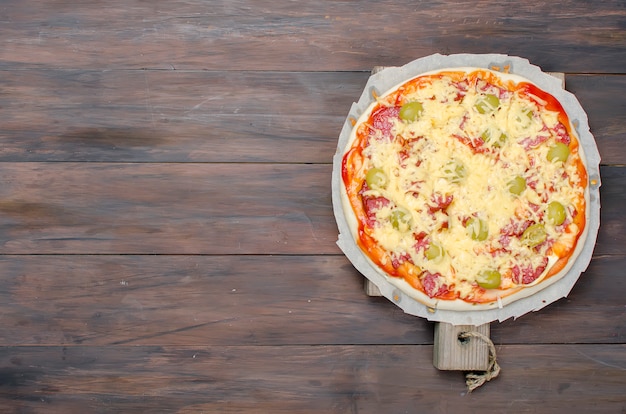 Tasty pizza  with spices and olives on a rustic old dark wooden table. copyspace