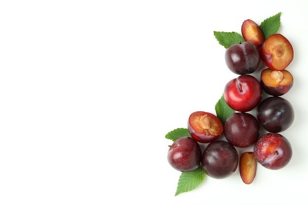 Tasty plums with leaves on white background.