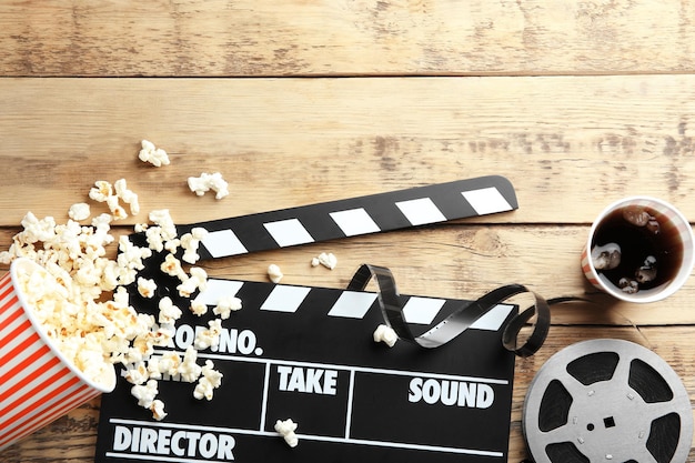 Tasty popcorn clapboard and movie reel on wooden background