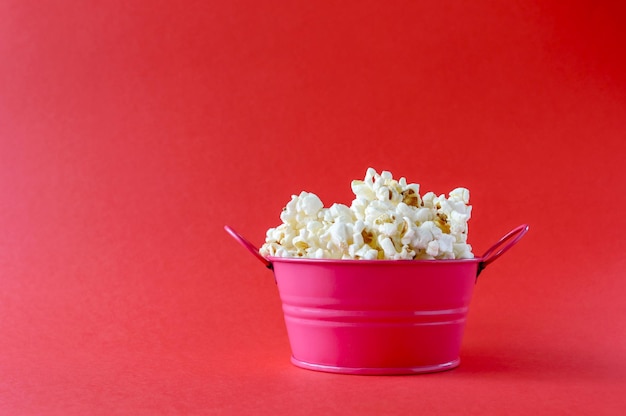Фото Вкусный попкорн в железной розовой миске на красном фоне