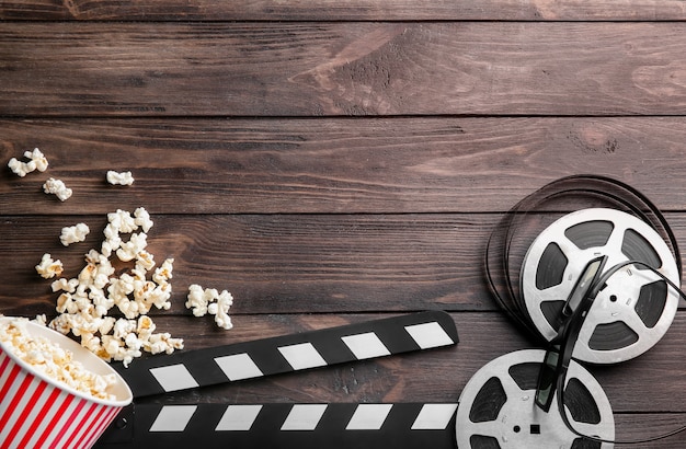 Tasty popcorn, movie reel and clapboard on wooden