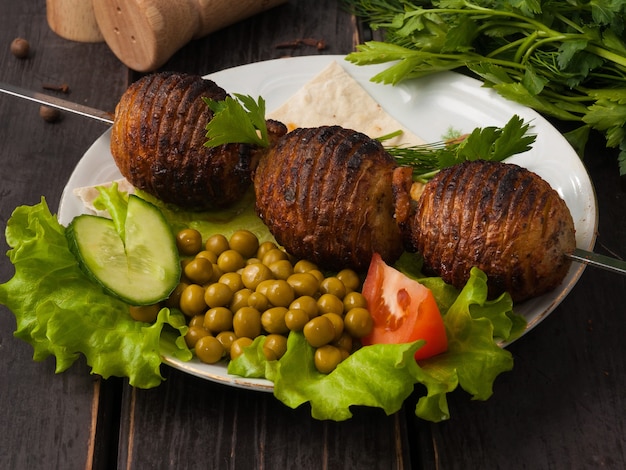 Photo tasty potatoes on coals on a skewer, decorated with green peas