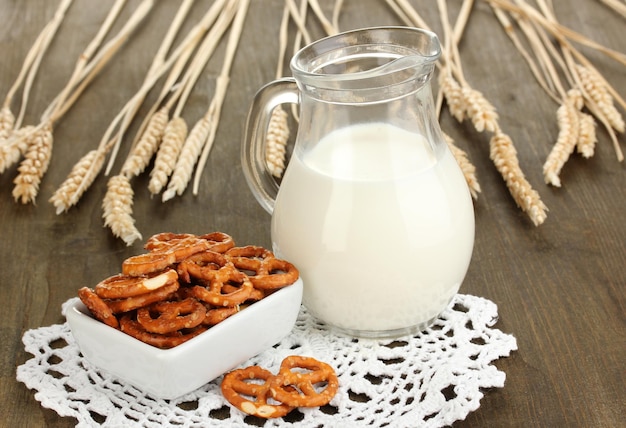 Tasty pretzels in white bowl and milk jug on wooden table closeup