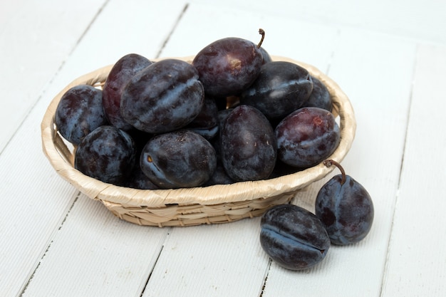 Tasty purple plums isolated on a white wooden background.