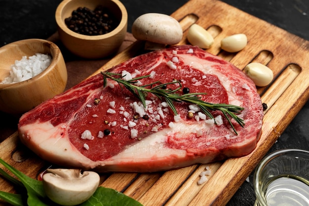 Tasty raw beef steak with salts, peppers, rosemary, garlics, and mushroom on a wooden board.