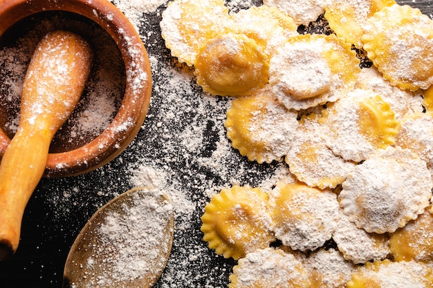 Tasty raw ravioli with flour and basil on wood table