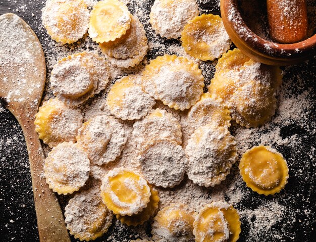 Tasty raw ravioli with flour and basil on wood table