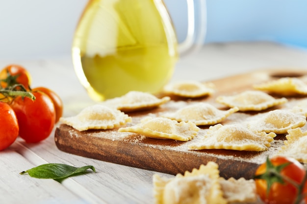 Tasty raw ravioli with flour, cherry tomatoes, sunflower oil and basil on a light wooden surface