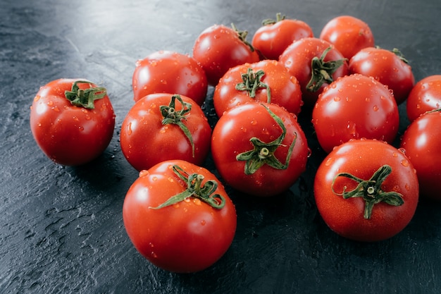 Tasty red ripe fresh tomatoes with water drops on dark background. Vegetables picked from garden. Domestic raw food. Close up shot.