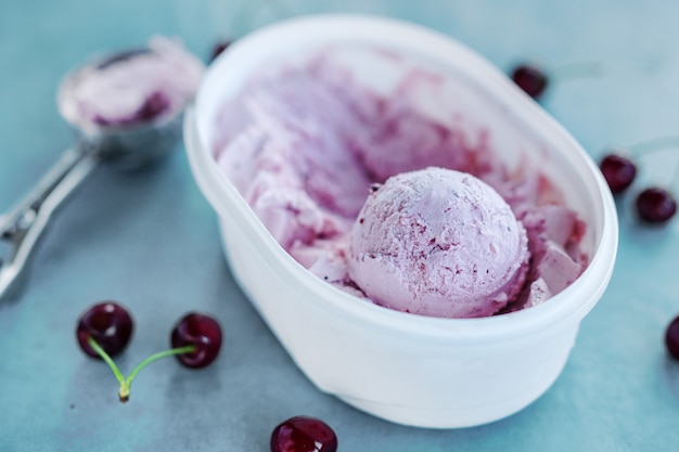 Tasty refreshing ice cream with cherry in plastic box on bright background.