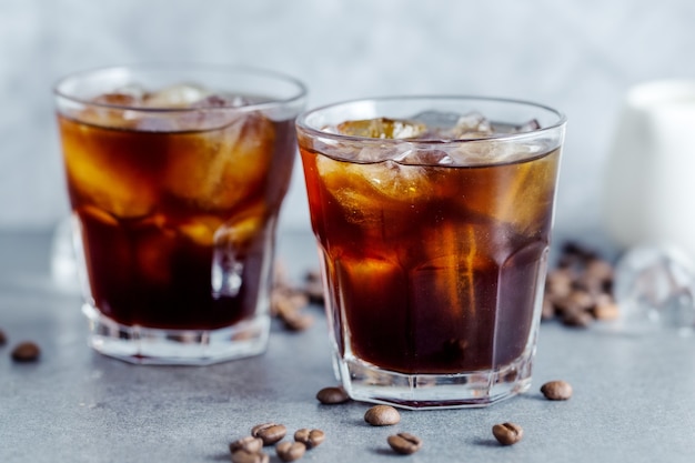 Tasty refreshing iced coffee with ice cubes in glasses on bright background. Closeup