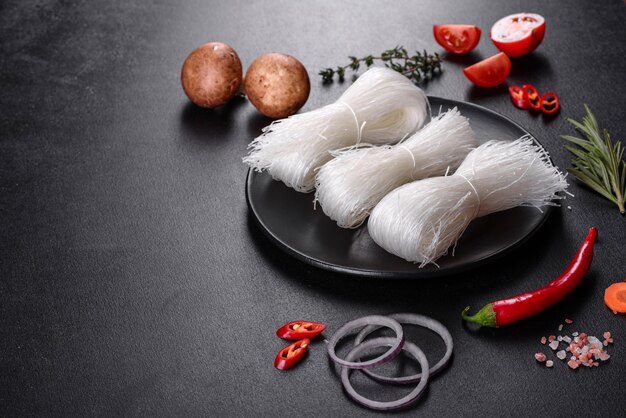 Tasty rice noodles with tomato, red pepper, mushrooms and seafood on a dark concrete background