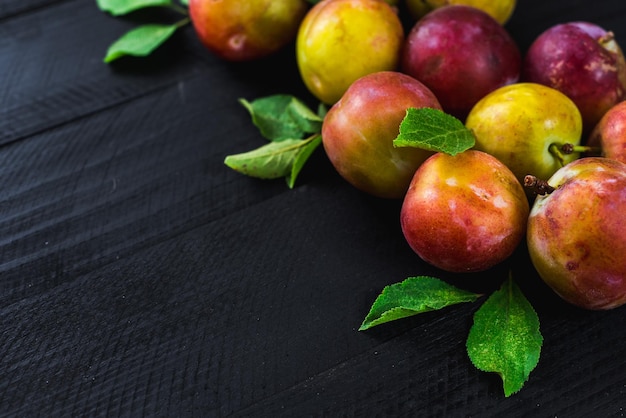 Tasty ripe plums on black wooden background. Copy space