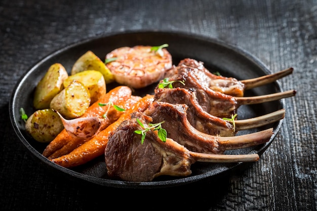 Tasty roasted lamb ribs with vegetables on dark background