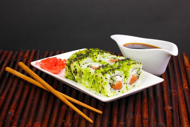 Photo tasty rolls served on white plate with chopsticks on bamboo mat on black background