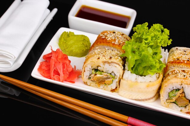 Tasty rolls served on white plate with chopsticks isolated on black