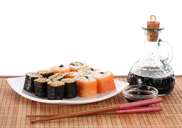 Tasty rolls served on white plate with chopsticks and soy sauce on bamboo mat isolated on white