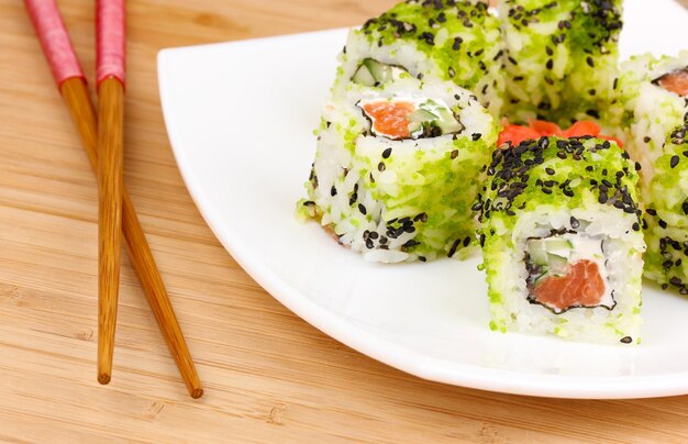 Tasty rolls served on white plate with chopsticks on wooden table closeup