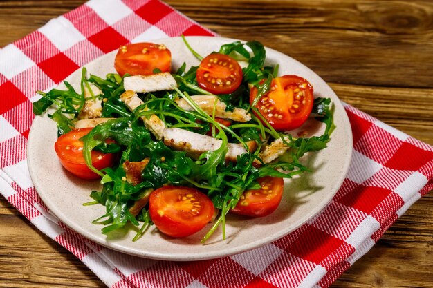 Tasty salad of fried chicken breast fresh arugula and cherry tomatoes on wooden table