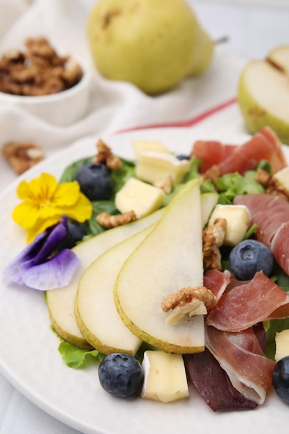 Tasty salad with brie cheese prosciutto walnuts and pear on white plate closeup