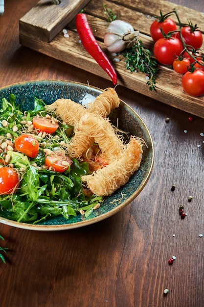 Фото Вкусный салат с креветками в тесте kataifi в зеленой миске на деревянном столе. композиция с салатом, соусами, помидорами и розмарином. крупным планом зрения. еда плоская планировка