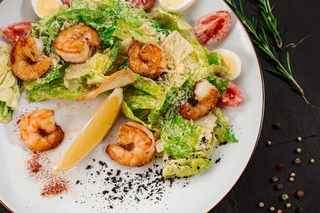 Tasty salad with shrimps herbs and vegetables on black background