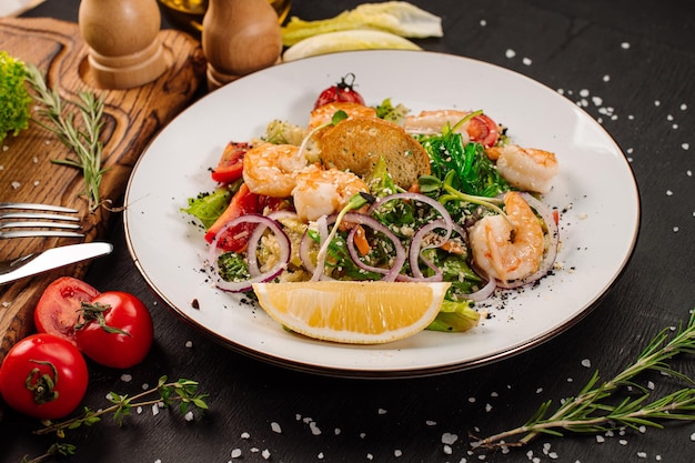 Tasty salad with shrimps herbs and vegetables on black background