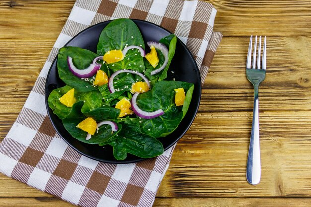 Tasty salad with spinach orange red onion and sesame seeds on wooden table Top view Healthy food or vegetarian concept