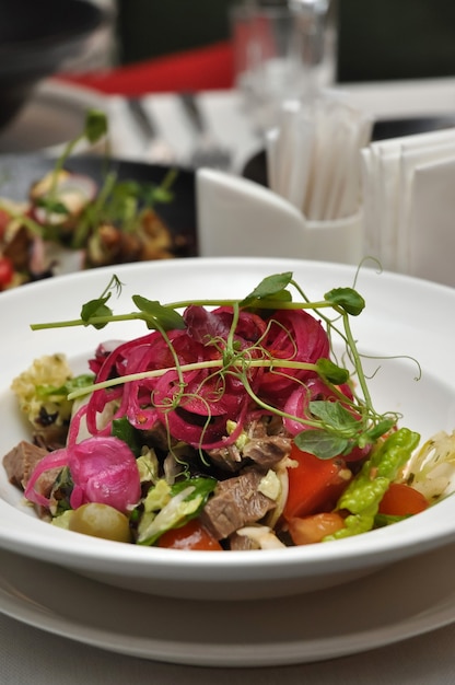 Tasty salad with vegetables and boiled beef on a white plate in a restaurant