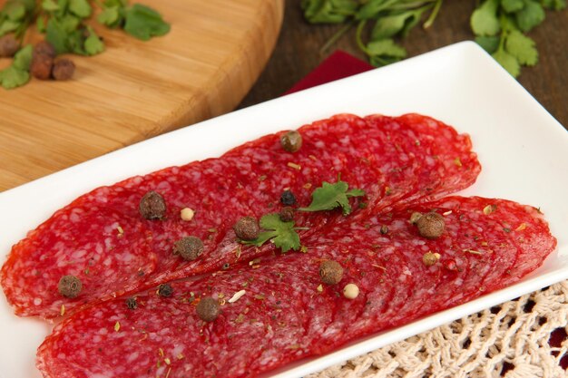 Tasty salami on plate on wooden table closeup