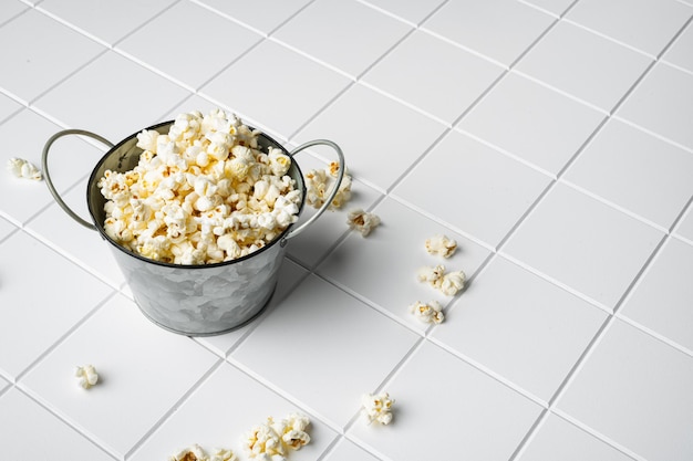 Tasty salted popcorn on white ceramic squared tile table background with copy space for text