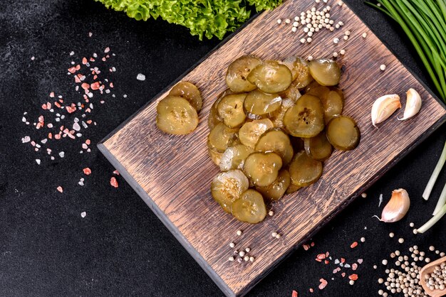 Tasty salty spicy pickled cucumber cut with rings on a wooden cutting board on a dark concrete background