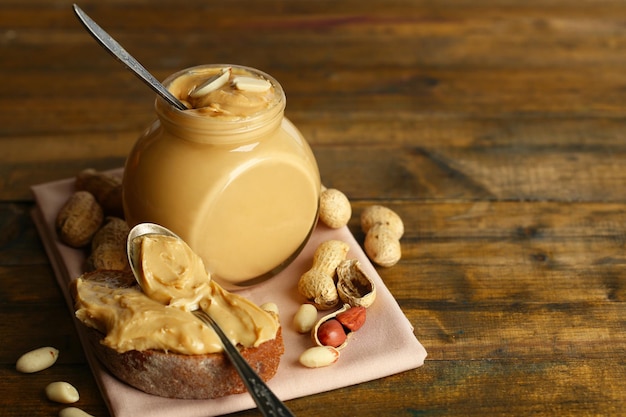 tasty sandwich and jar with fresh peanut butter on wooden background