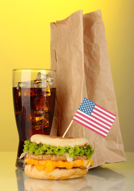 Tasty sandwich with american flag cola and package on yellow background