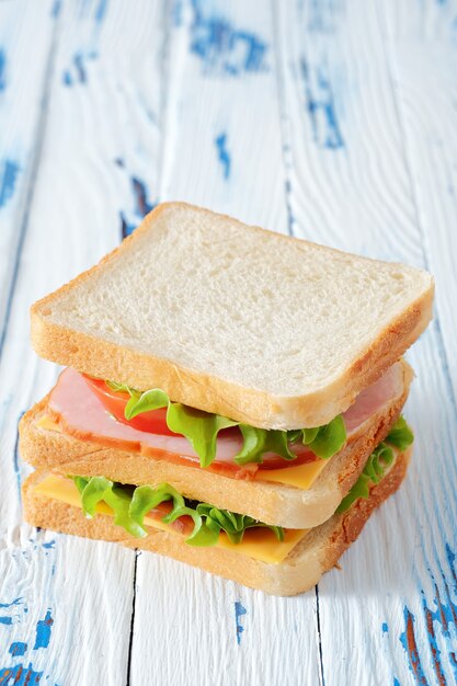 Tasty sandwich with ham, salad, cheese and tomatoes on rustic wooden table, close-up view, vertical orientation