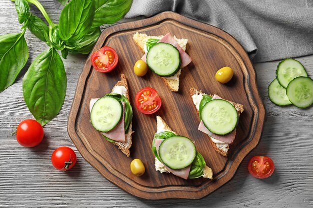 Tasty sandwiches with fresh cucumber on wooden board