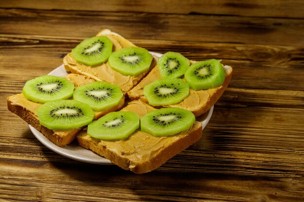 Tasty sandwiches with peanut butter and kiwi fruits on wooden table