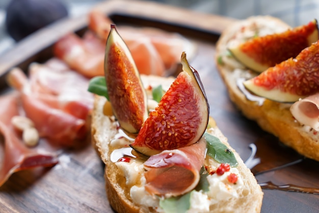 Tasty sandwiches with ripe fig and prosciutto on wooden board, closeup