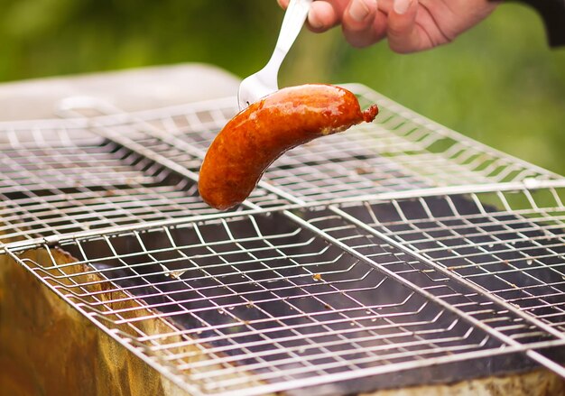 Tasty sausages frying on brazier with hot coals outdoors in the countryside at summer Cooking process Barbecue grill