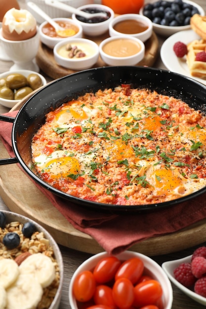 Вкусная шакшука на сковородке и другие блюда, подаваемые на завтрак на деревянном столе